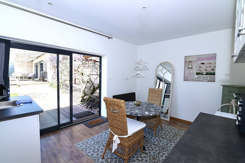 Dining area with a table and chairs, a mirror, a sink, and a sliding glass door leading to a balcony with a view of the garden.