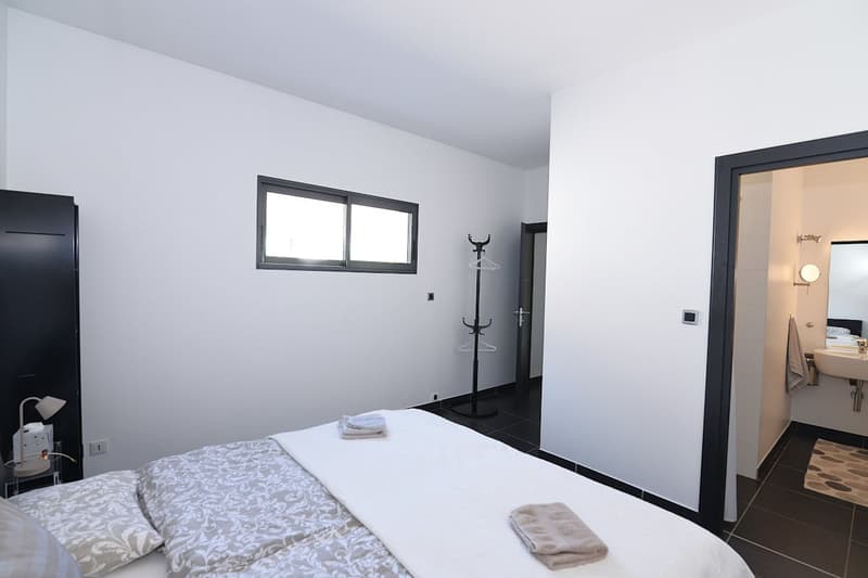 bedroom with a double bed, white walls, black tiled floor, window, lamp, wardrobe, bathroom with sink and mirror