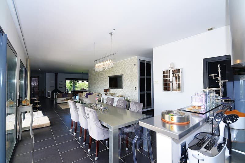 Dining room with a large table, chairs, chandelier, kitchen with appliances, and a television