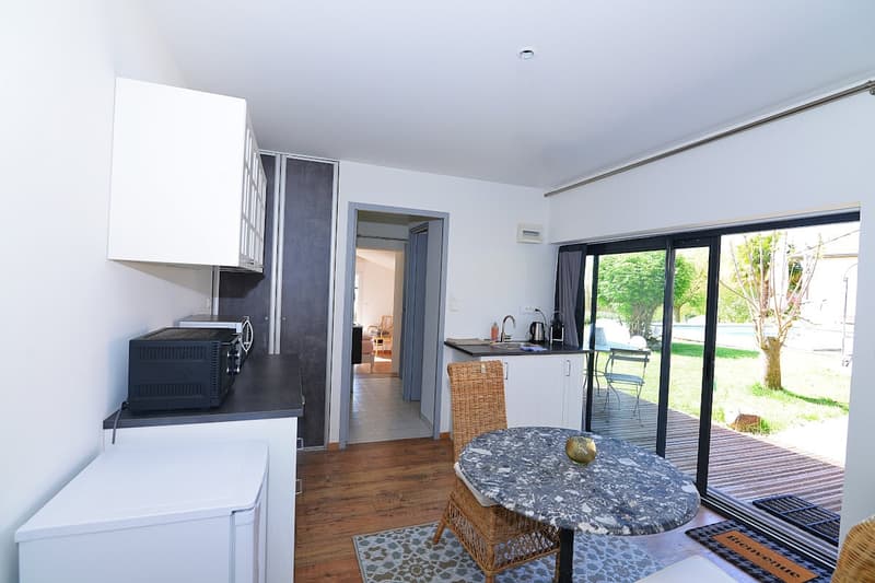 kitchen with dining area, wooden floor, white cabinets, microwave, sink, table, chairs, sliding glass doors, outdoor deck, grassy area, trees