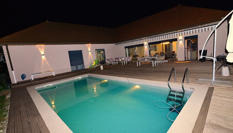 House with wooden deck, swimming pool, lounge chairs, tables, and lights