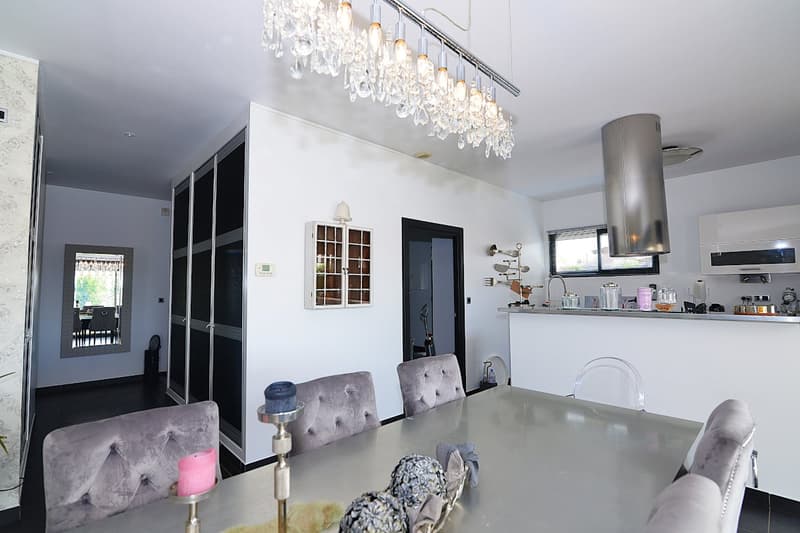 Dining room with a large table, chairs, chandelier, kitchen area with a counter, and a mirror