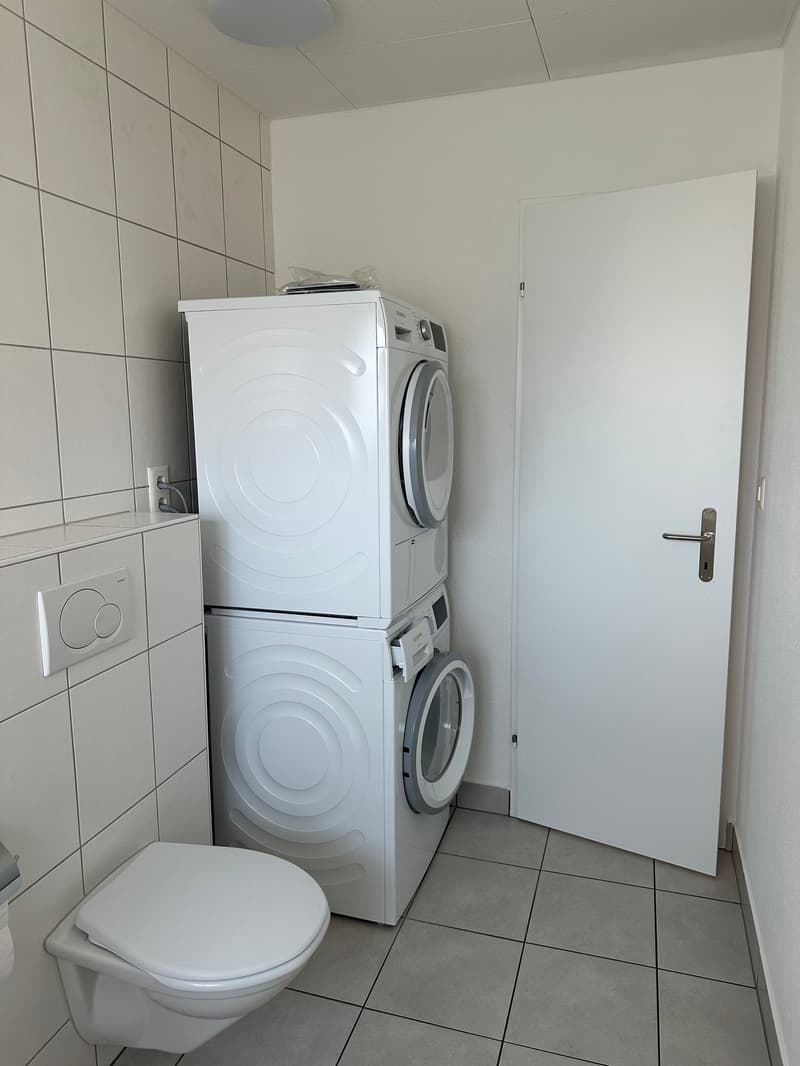 small bathroom with toilet, washing machine, dryer, white tiles