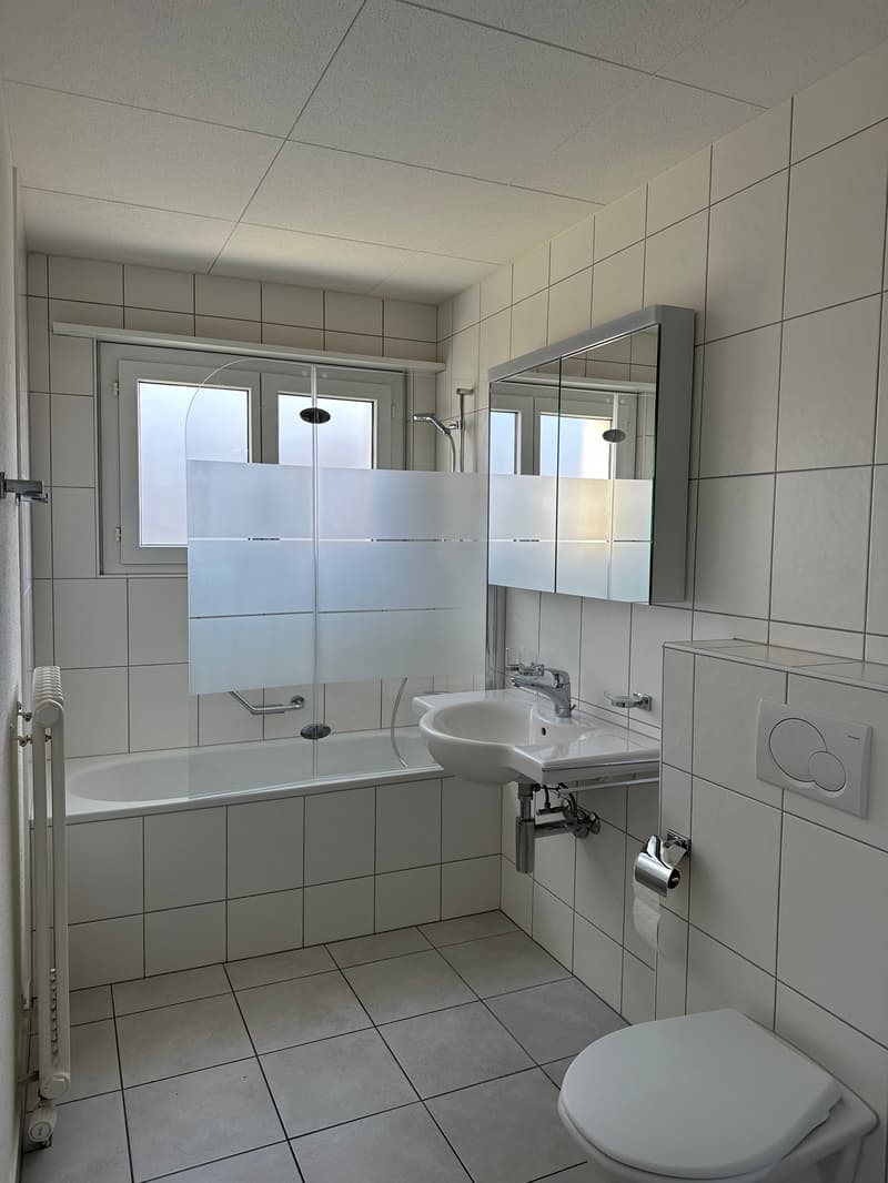 Bathroom with white tiles, sink, mirror, bathtub, and toilet. White shower curtain and faucet. No visible features.