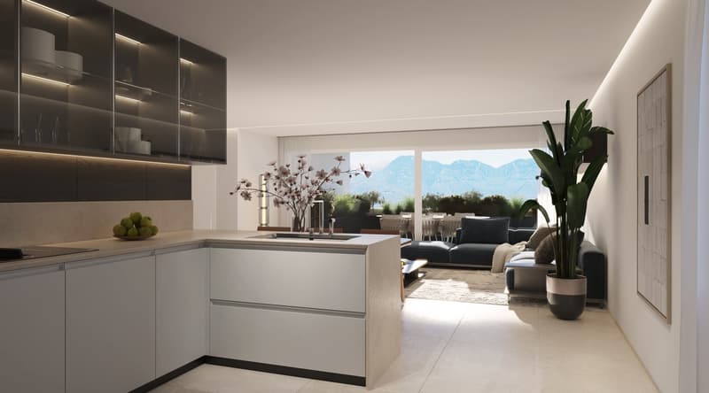 Modern, open-concept kitchen and living room with large windows overlooking a scenic outdoor view. The kitchen features sleek, dark cabinets and a central island. The living room has a comfortable sofa and chairs, with a potted plant adding a touch of gre