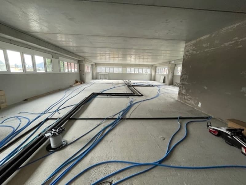 Large open space with concrete floor, exposed ceiling, and various electrical wires and cables running across the floor.