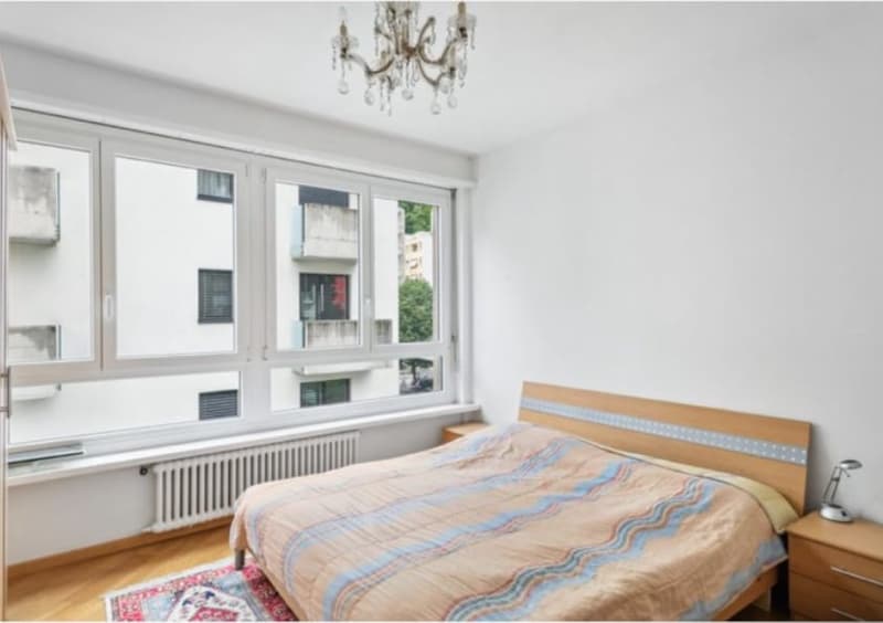 Large bed, bedside tables, chandelier, large windows, white walls, wooden floor, white radiators