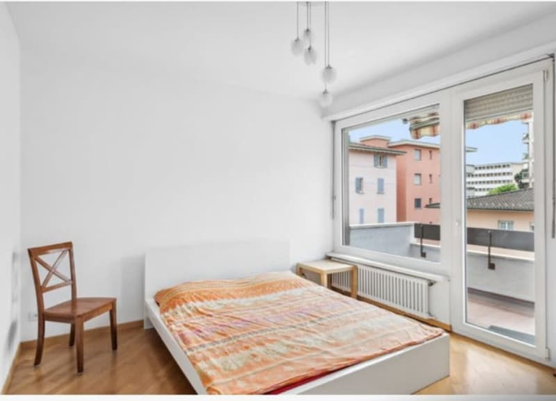 wooden floor, white walls, bed, chair, nightstand, large window with balcony view