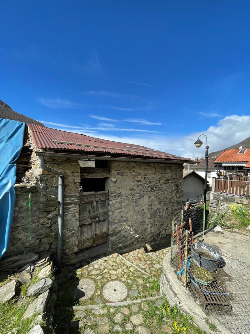 old stone house, red roof, wooden door, fenced area, mountains in the background