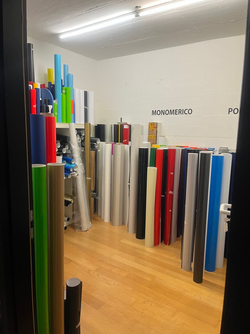 Rows of cylindrical objects organized by color, white wall with text, ceiling lights, wooden floor
