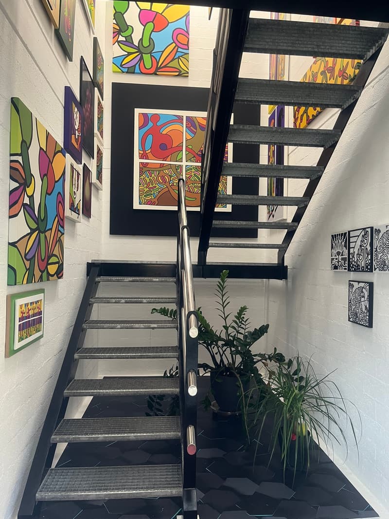Staircase in the hallway with metallic railing, hexagon floor tiles, colorful paintings on the walls