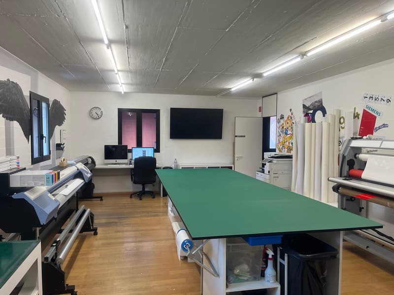 printing office with large tables, printers, computers, storage, window, clock, closed door