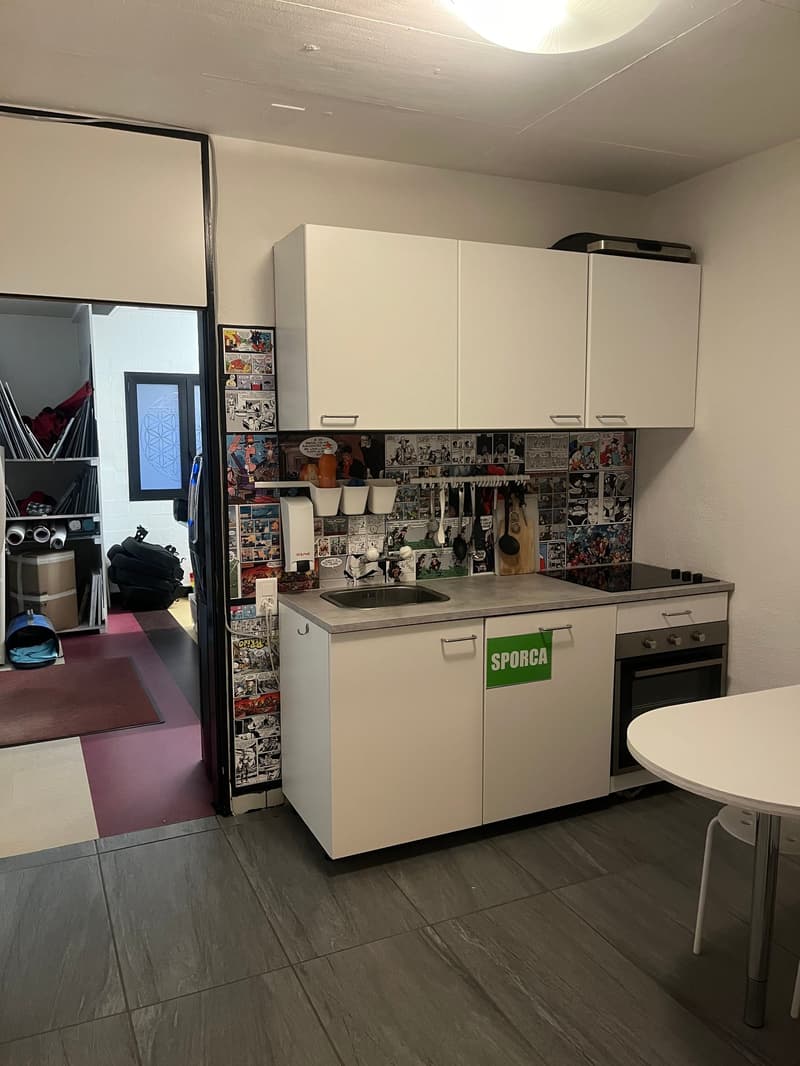 small kitchenette with sink, stove, and microwave, white cabinets, tiled floor, round white table, white chair, magazine rack