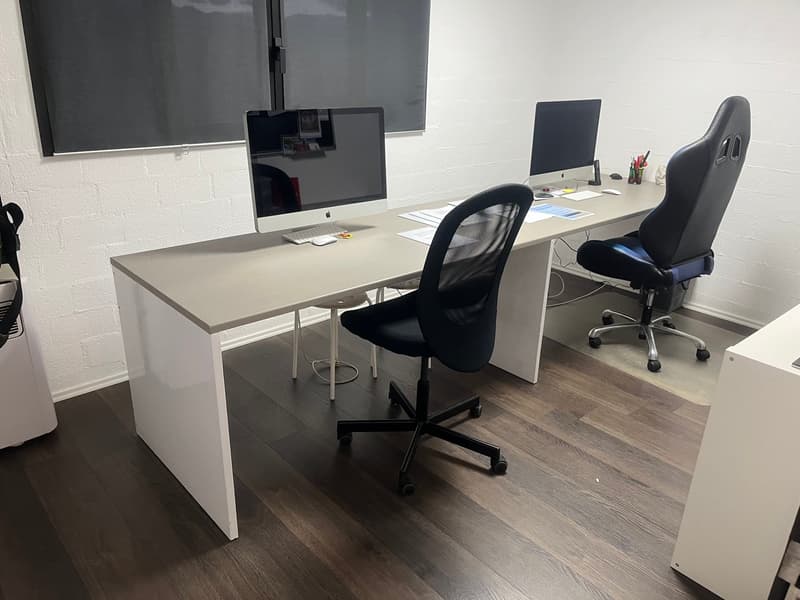 A workstation with desks, computers, chairs, and a large monitor on the wall.