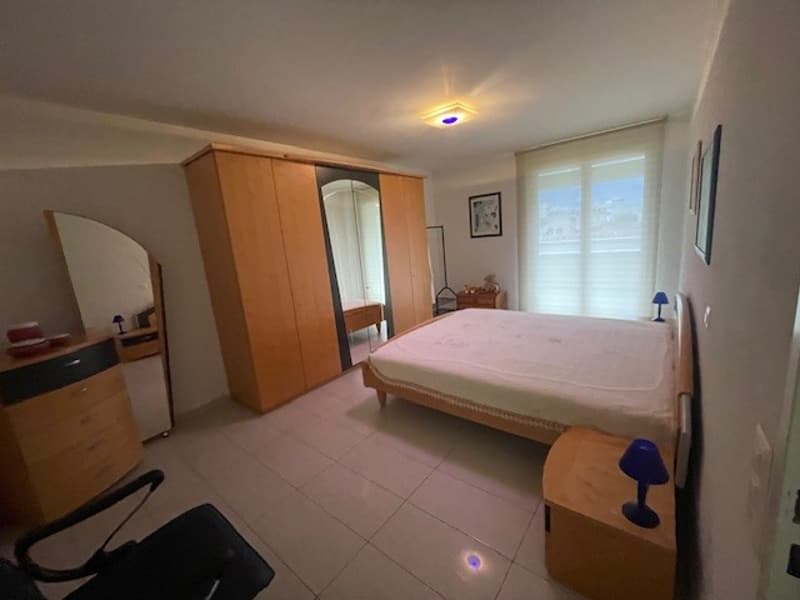 Bedroom with a bed, large mirror, wooden cabinet, nightstand, and a chair.