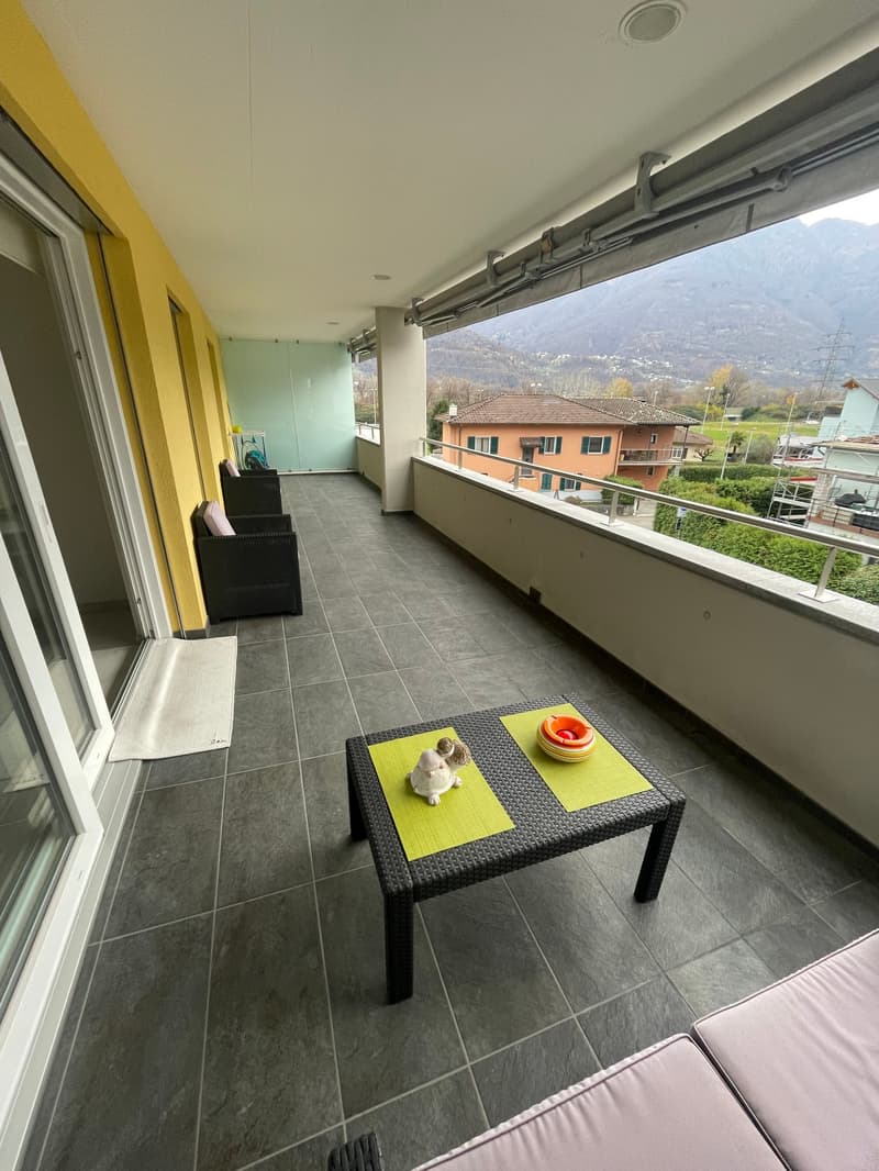 Terrace with yellow flooring, black furniture, table with white figures, surrounded by metal railing, a scenic mountain view.