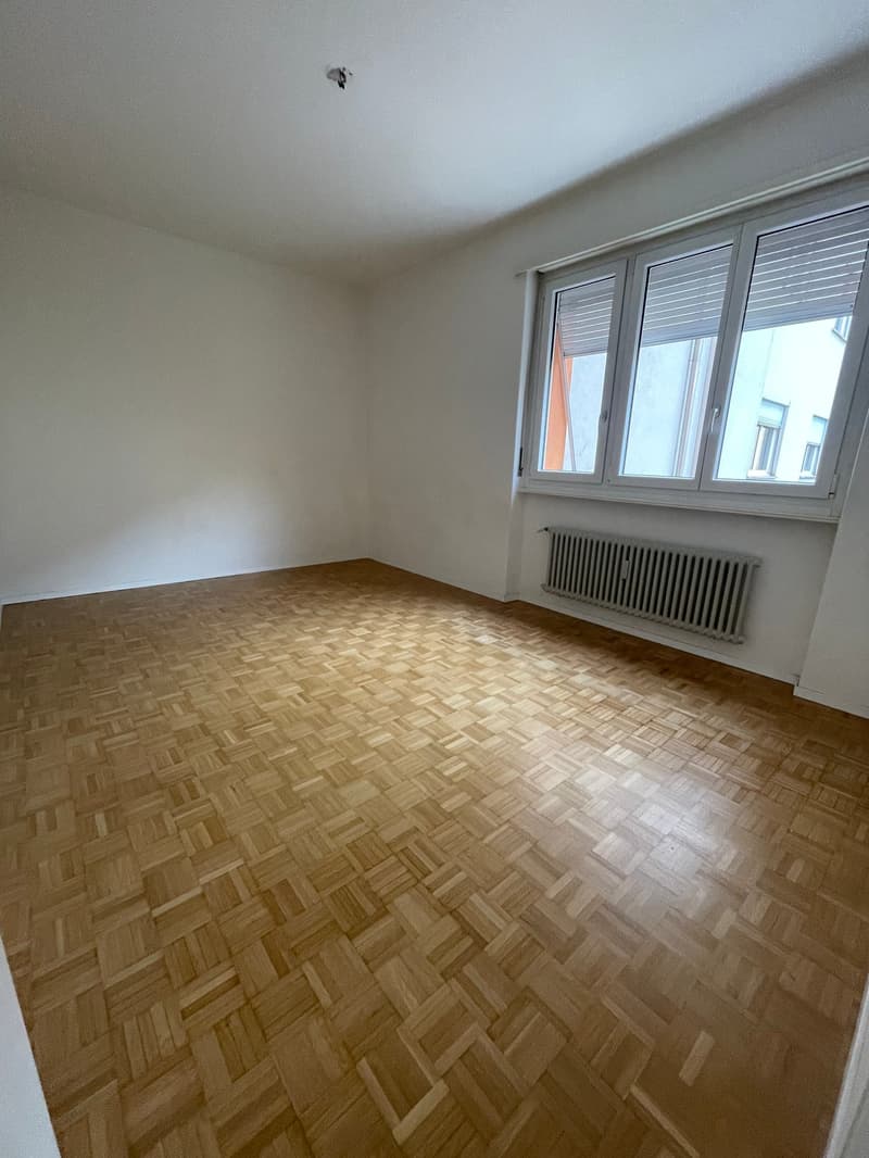 Empty room, wooden parquet flooring, large window, white walls, white ceiling, underfloor heating