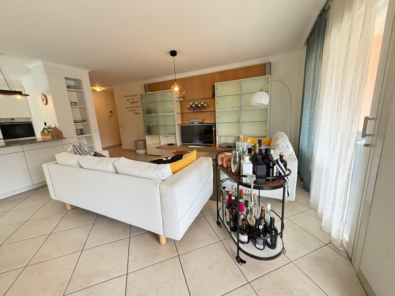 modern living room with white couches, tiled floor, glass shelves, TV, and a bar cart with bottles