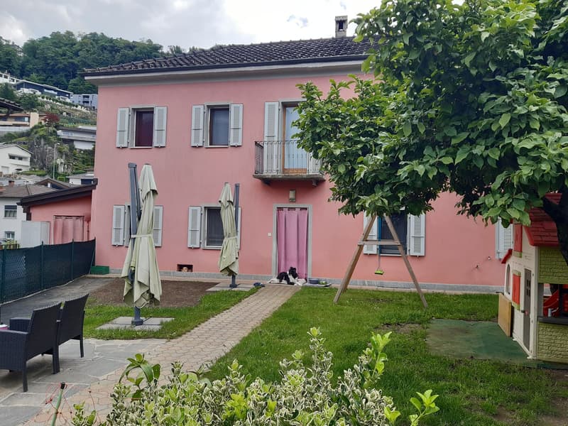 2-story pink house with shuttered windows, balcony, and a small yard with a paved walkway, garden, and outdoor furniture