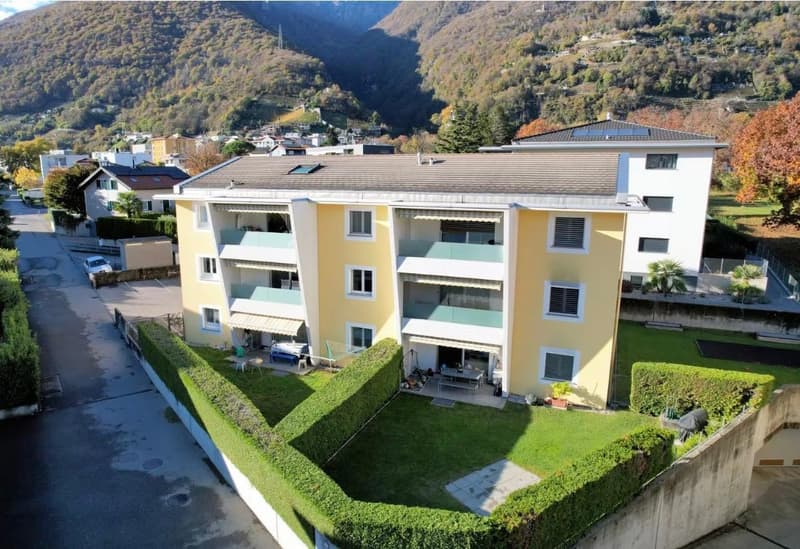 3-story apartment building, yellow exterior, multiple balconies, green hedges, solar panels on the roof, mountain view