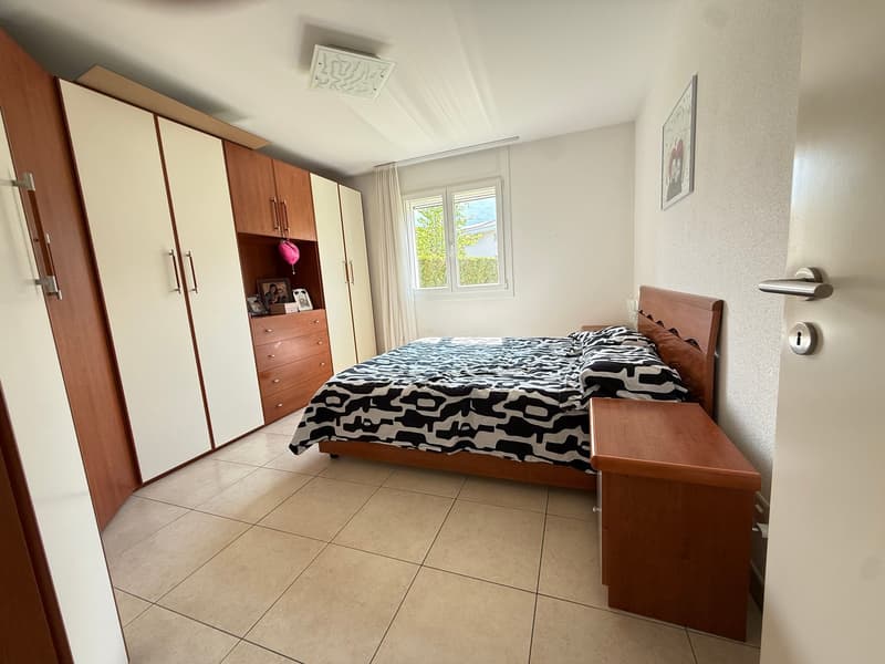 Bedroom with wooden bed, white and brown wardrobes, wooden nightstand, tiled floor, window with curtains, picture frame on the wall