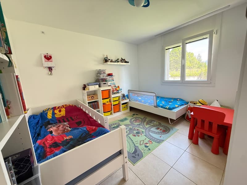 Children's room with two beds, toys, shelves, rug, and a desk with a chair