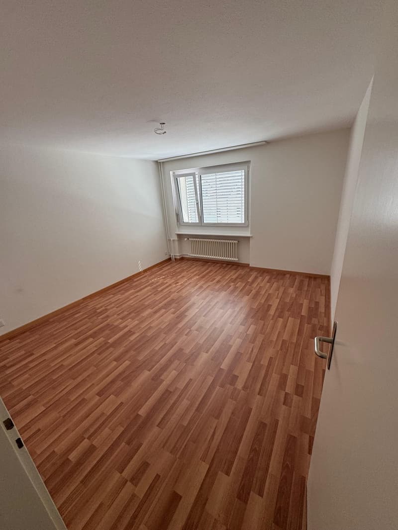 Empty room with wooden floor, white walls, a window, and a white radiator