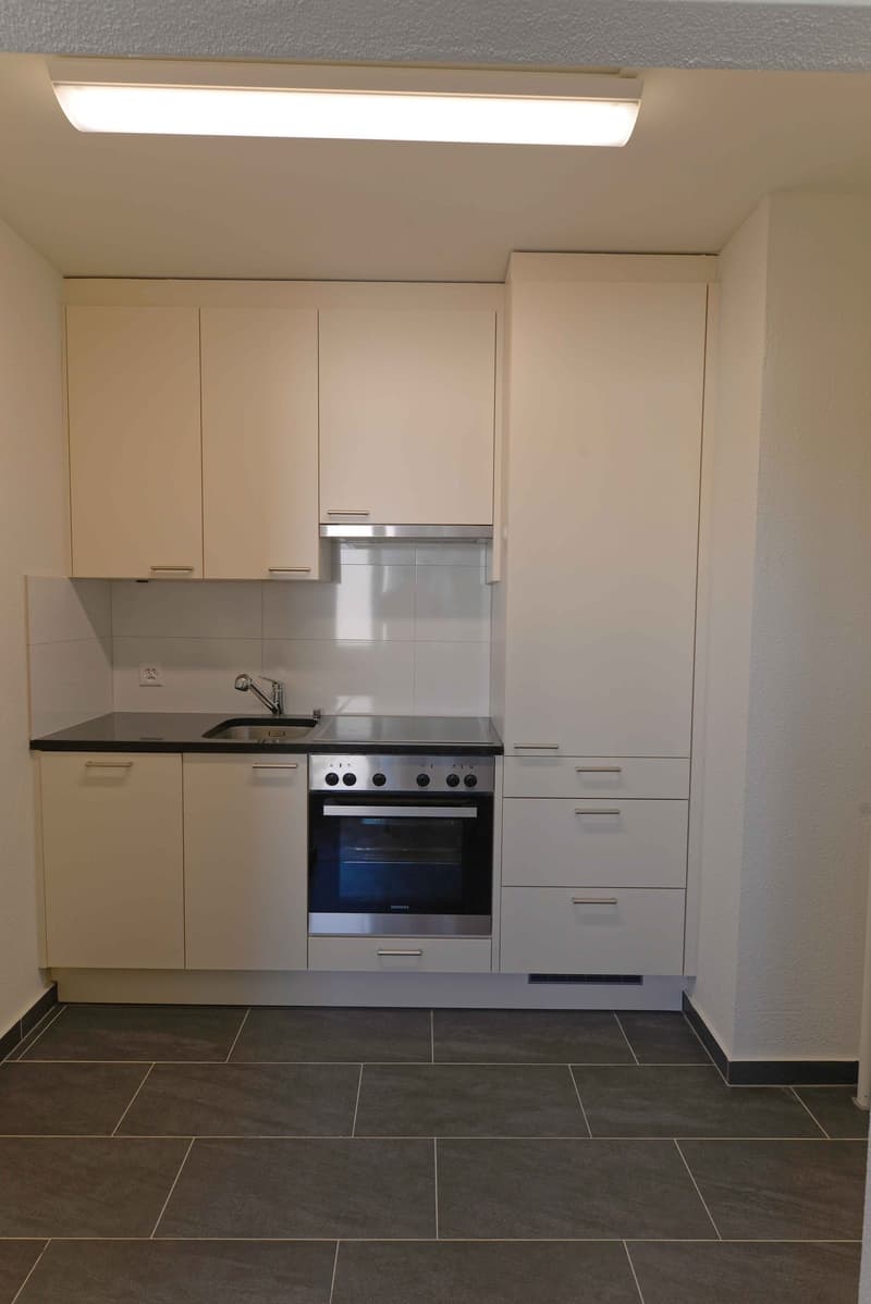 modern kitchen with white cabinets, black countertop, stainless steel oven, sink, faucet, and tiled floor