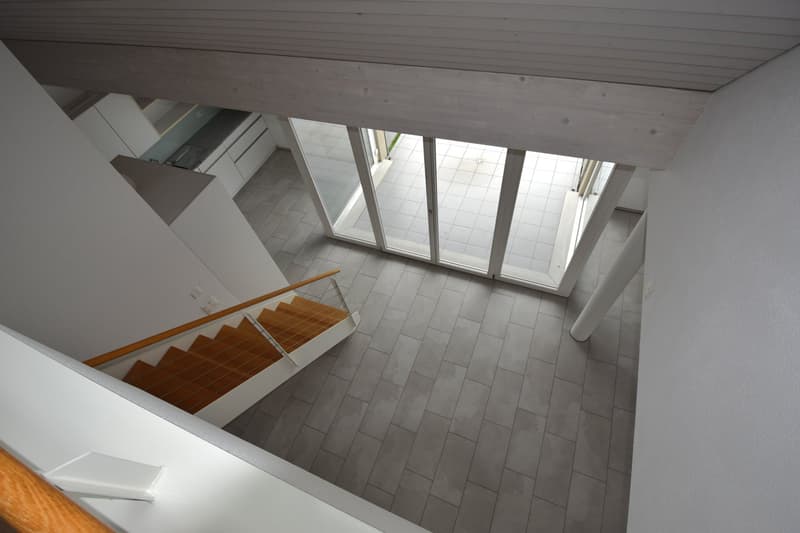 Modern interior with open floor plan, wooden staircase, glass sliding doors leading to terrace, tile flooring, and white walls.