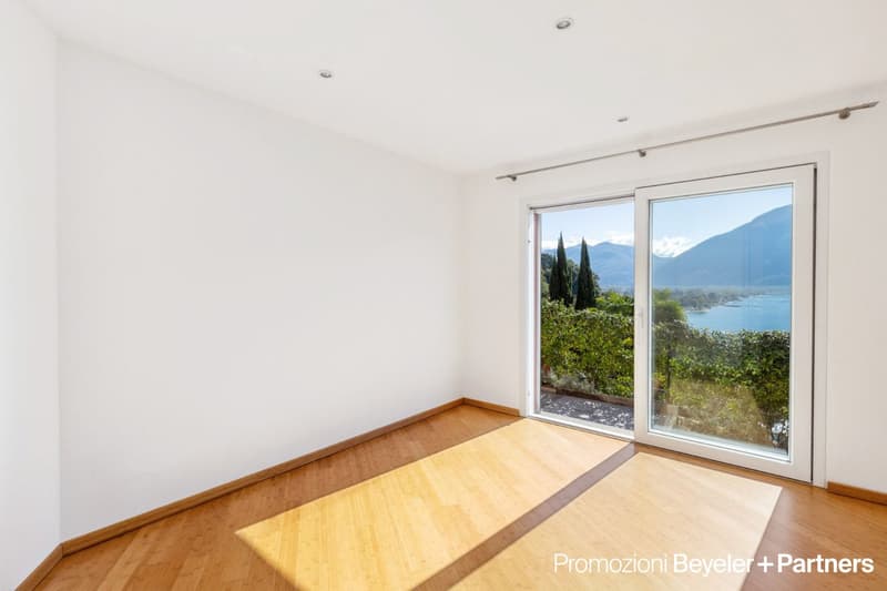 Modern room with white walls and bamboo floors, large sliding glass doors providing lake view, minimalistic decor.