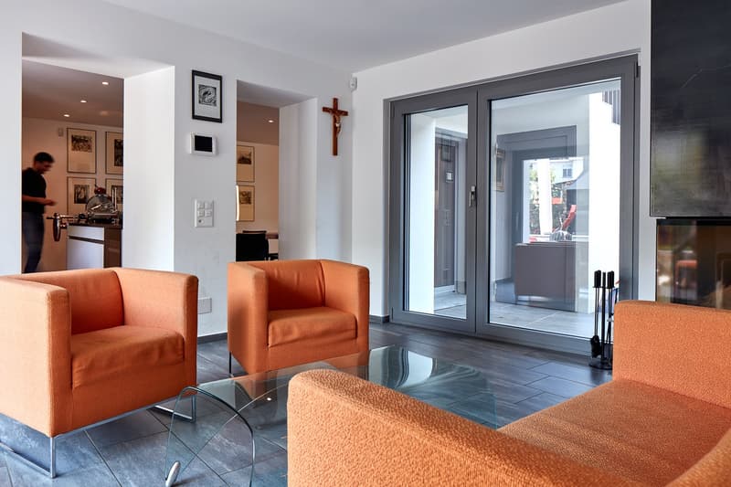 modern living room with orange chairs, glass table, fireplace, sliding glass doors