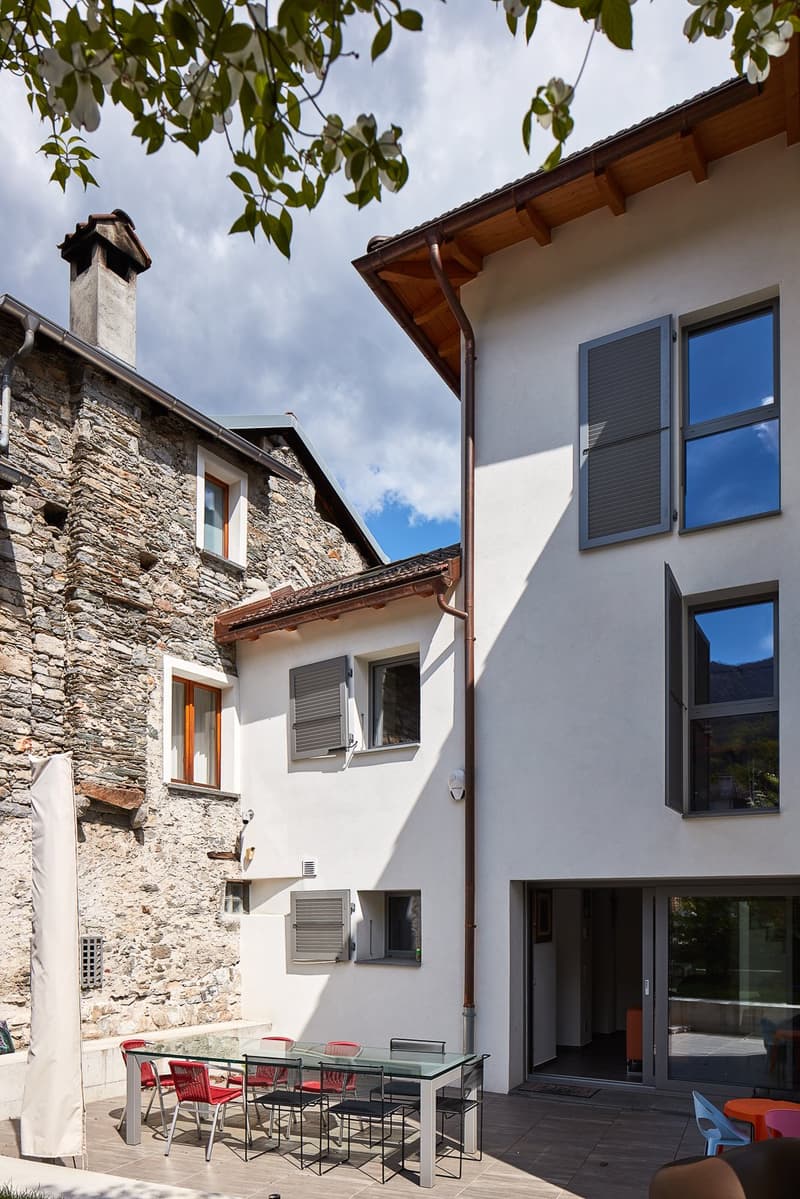 Two-story house with stone and white walls, multiple windows, a glass table and chairs, and a chimney