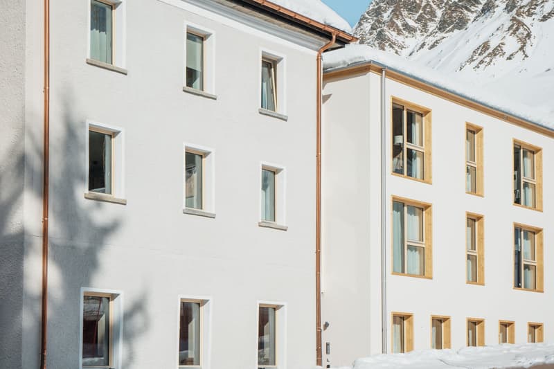 Modern white building with many windows, snowy roof, mountains in the background, two stories, white exterior, wooden accents