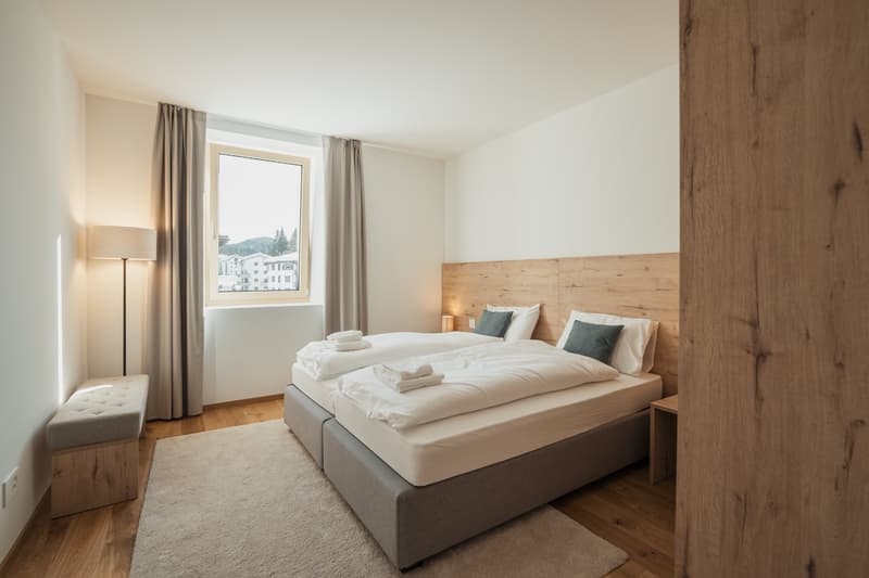 Spacious bedroom with large window offering a scenic view, wooden headboard, grey bedding, and a cozy rug on the hardwood floor.