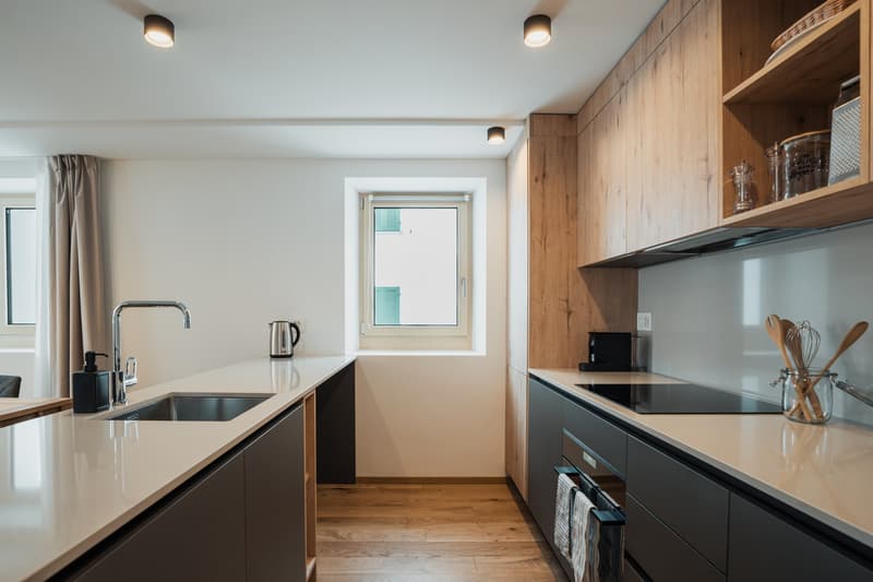 Modern kitchen with wooden floors, white countertops, large sink, and ample cabinet space.