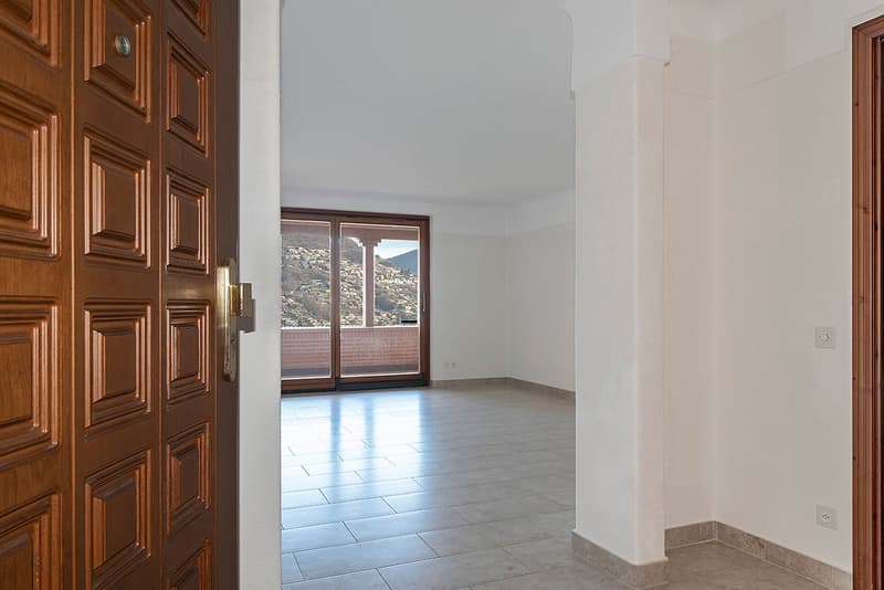 Large room with wooden paneled doors, tile flooring, and a sliding glass door leading to a balcony or terrace with a view of the mountains.
