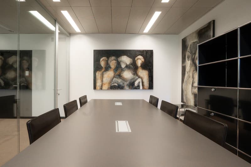 Large conference table with black leather chairs, abstract painting on the wall, glass walls, and modern lighting fixtures on the ceiling.
