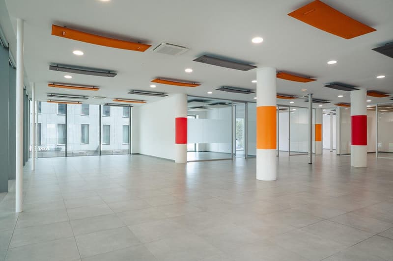 Empty room with glass walls, tiled floors, white ceiling, multiple columns with red and orange stripes.