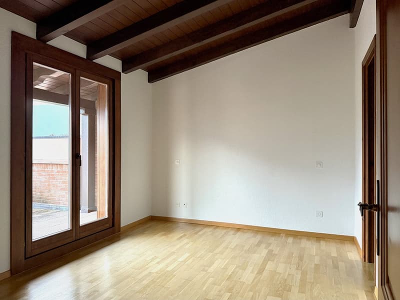 wooden floor, large glass doors leading to a balcony, white walls, power outlets, ceiling with wooden beams