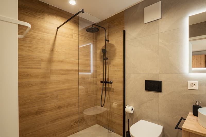Modern bathroom with wooden walls, glass shower enclosure, white toilet, and a wooden countertop with a sink and soap dispenser.