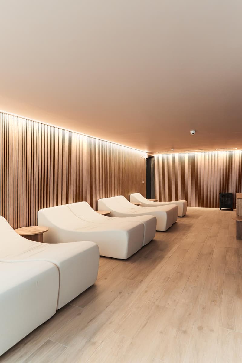 A room with white lounge chairs, wooden side tables, and wooden flooring. The walls are made of vertical wooden panels.