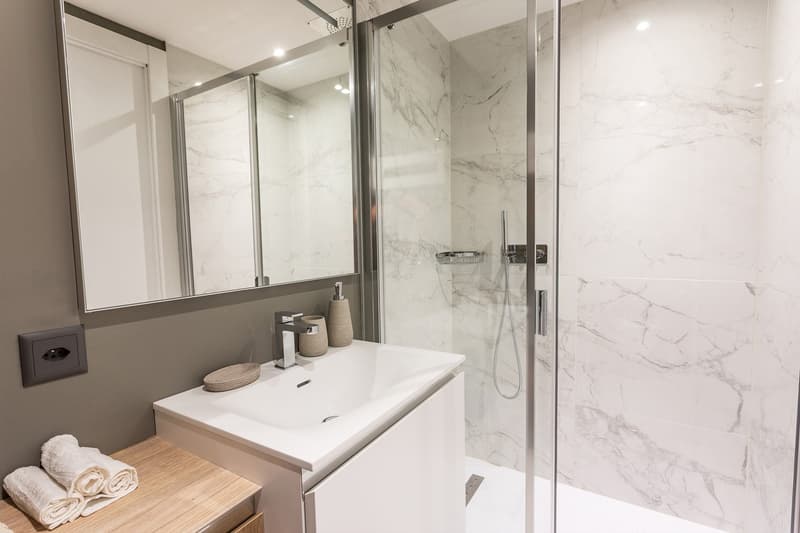 Modern bathroom with marble-like tiles, glass shower enclosure, white vanity with sink, and towels