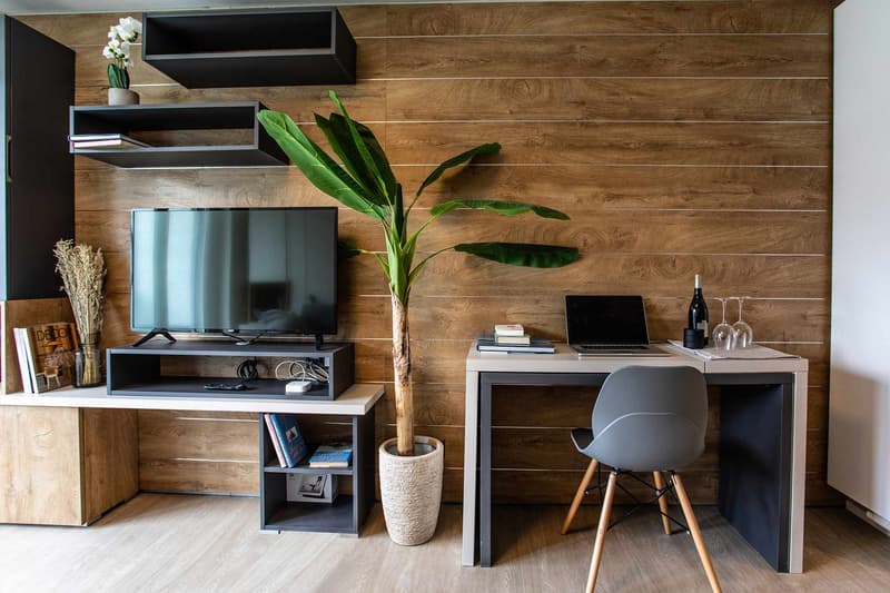 Wooden wall panels, TV stand with shelves, laptop on desk, potted plant, wooden chair