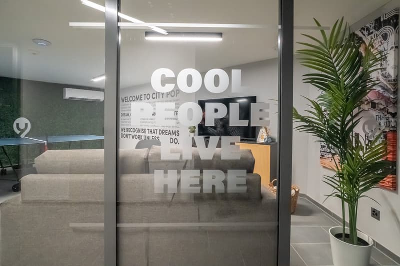 Modern office space with large windows, palm plant, and a welcome sign that says 'Cool people live here' on the glass wall.