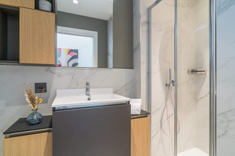 Modern bathroom with marble-like tiles, a white sink vanity with a black countertop, a shower enclosure, and built-in storage cabinets.