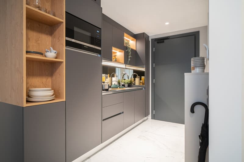 Modern kitchen with gray cabinets, built-in appliances including a dishwasher, open shelving, and a marble-like countertop. The kitchen has a clean, minimalist design with a mix of wood and gray tones.