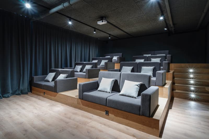 Dark, theater-style room with gray upholstered seating, wood flooring, and a projector screen or display at the front