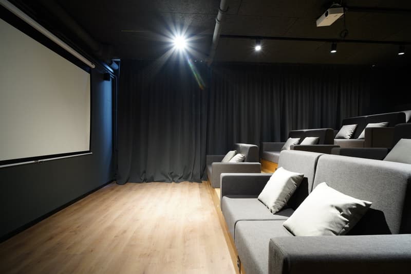 Dark room with a large projection screen, comfortable gray sofas and chairs, and recessed lighting providing a cozy and immersive home cinema experience.