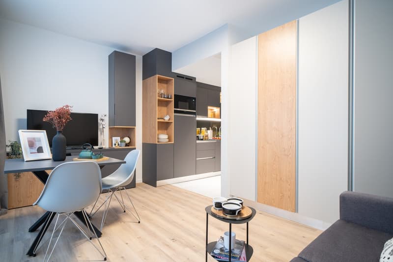 Modern kitchen with gray cabinets, wooden shelves, built-in appliances, and a dining area with a table and chairs