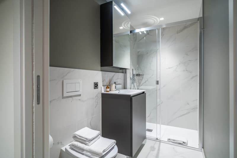 Modern bathroom with marble-like tiles, black vanity cabinet, white sink, glass shower enclosure, and towels
